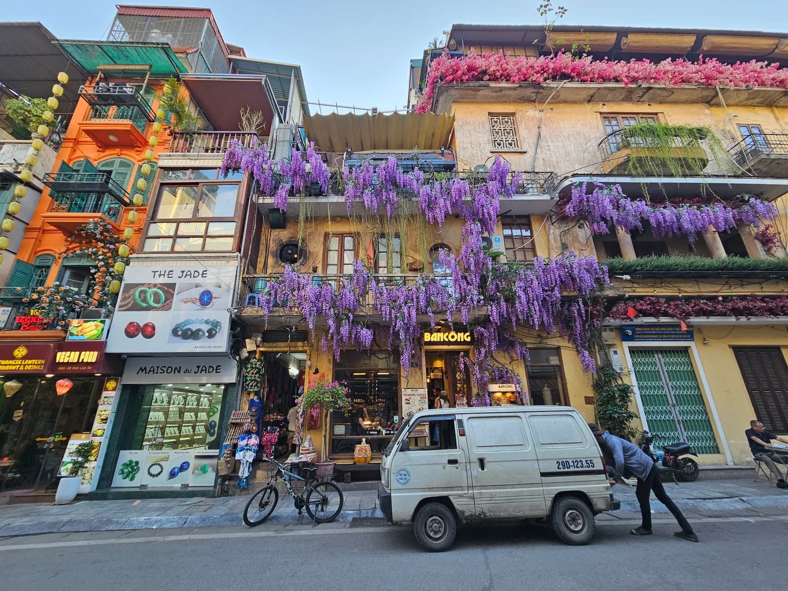 Shopfronts on a Hanoi street hung with wisteria, a white van parked outside